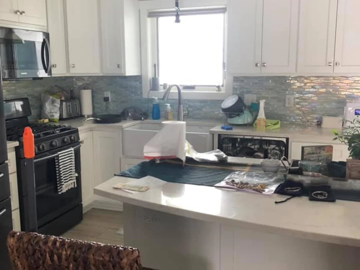 a kitchen with clutter and residue across the counters and island before professional house cleaning