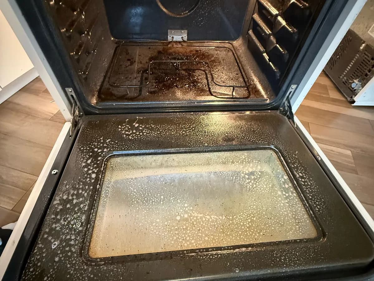 grease and baked-on residue inside an oven and across its door before property-management cleaning in British Columbia