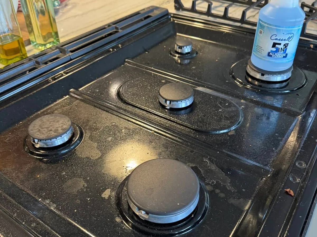 grease and cooking residue on a black gas stovetop before professional house cleaning